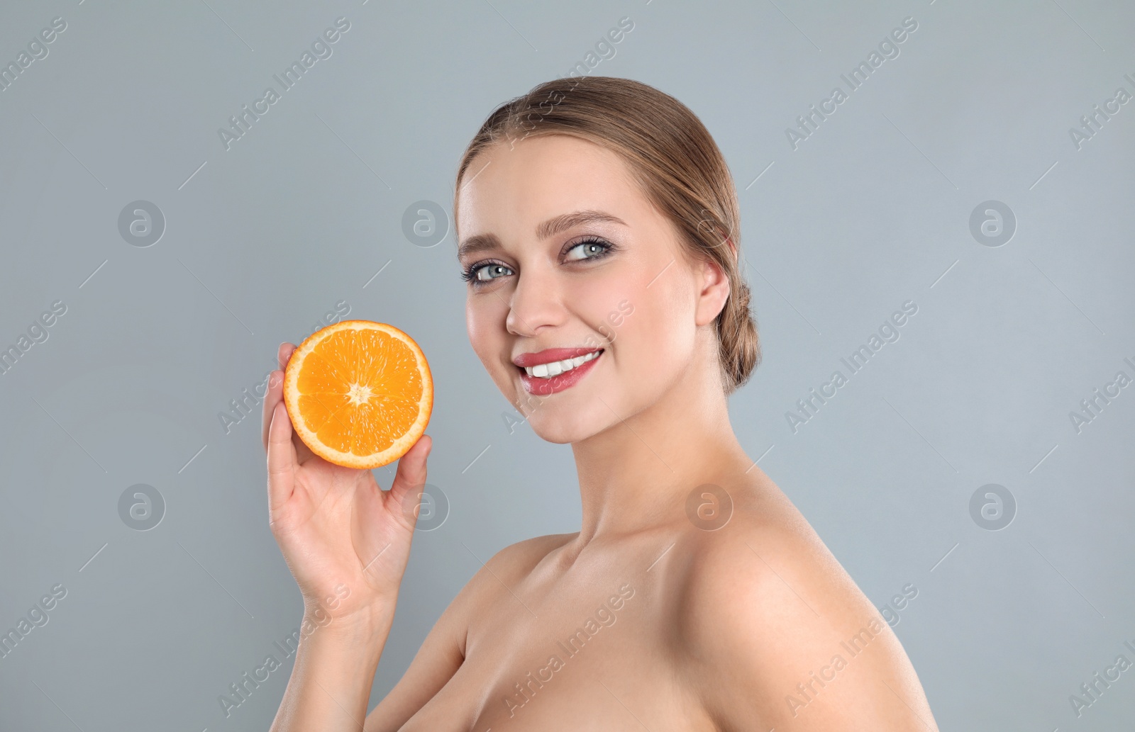 Photo of Young woman with cut orange on grey background. Vitamin rich food