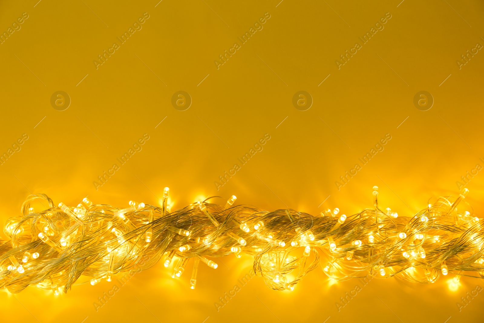 Photo of Glowing Christmas lights on yellow background, top view. Space for text