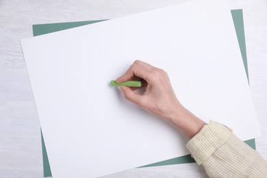 Woman drawing on paper with pastel at white wooden table, top view