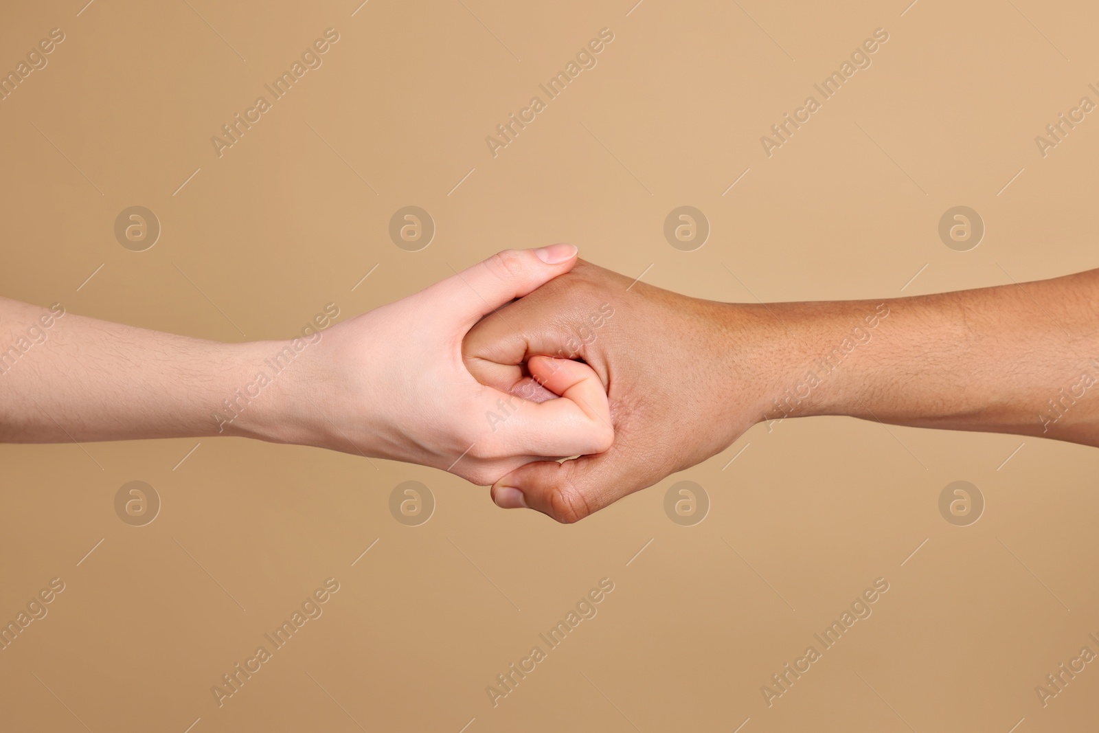 Photo of International relationships. People strongly joining hands on light brown background, closeup
