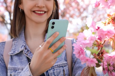 Photo of Young woman taking picture of blossoming sakura tree branch in park, closeup
