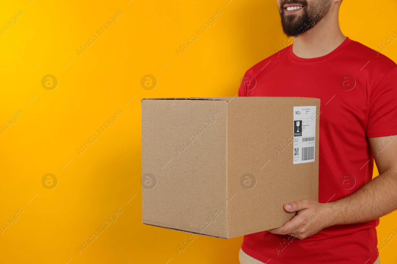 Photo of Courier holding cardboard box on yellow background, closeup. Space for text