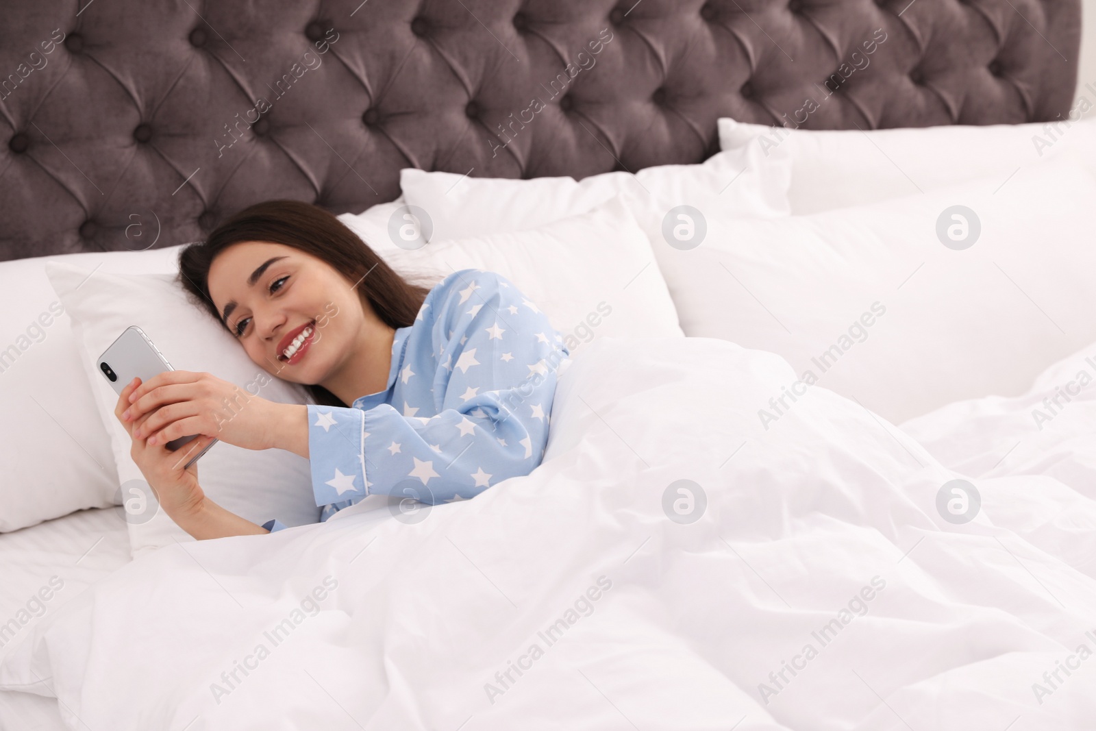 Photo of Young woman addicted to smartphone in bed at home