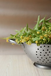 Beautiful linden blossoms and green leaves in metal colander on white wooden table, closeup