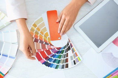 Photo of Woman with paint color palette samples and tablet at table, top view
