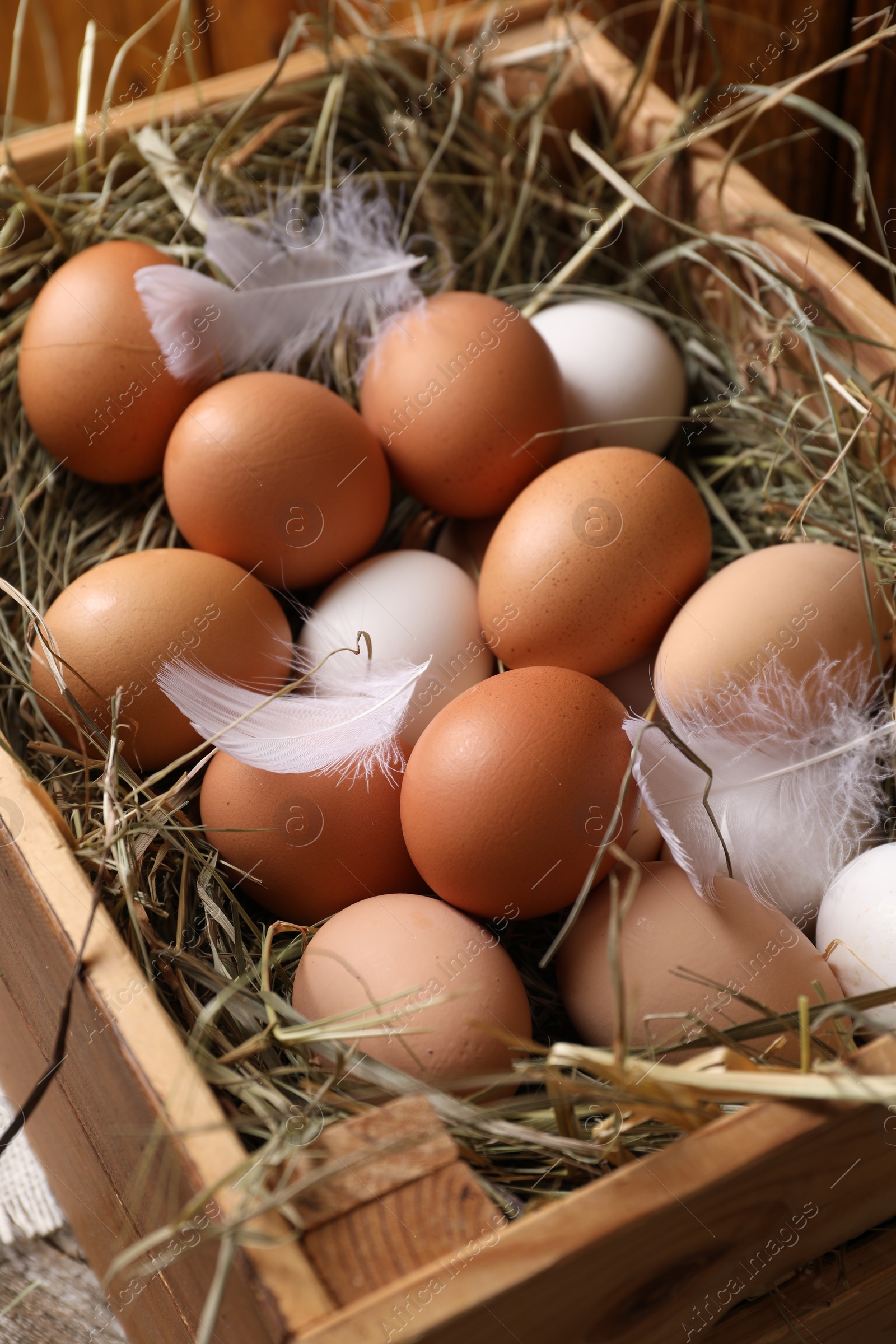 Photo of Fresh chicken eggs and dried hay in wooden crate, closeup