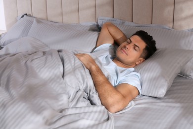 Man sleeping in comfortable bed with light grey striped linens