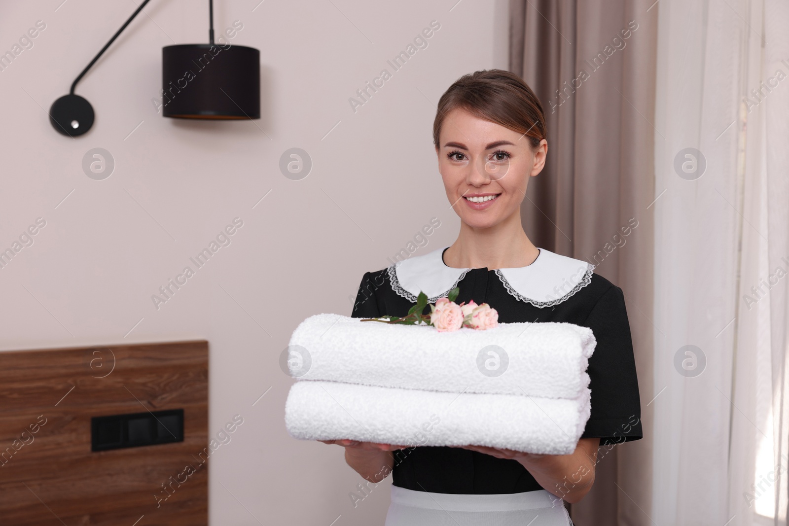 Photo of Beautiful chambermaid with stack of fresh towels in hotel room