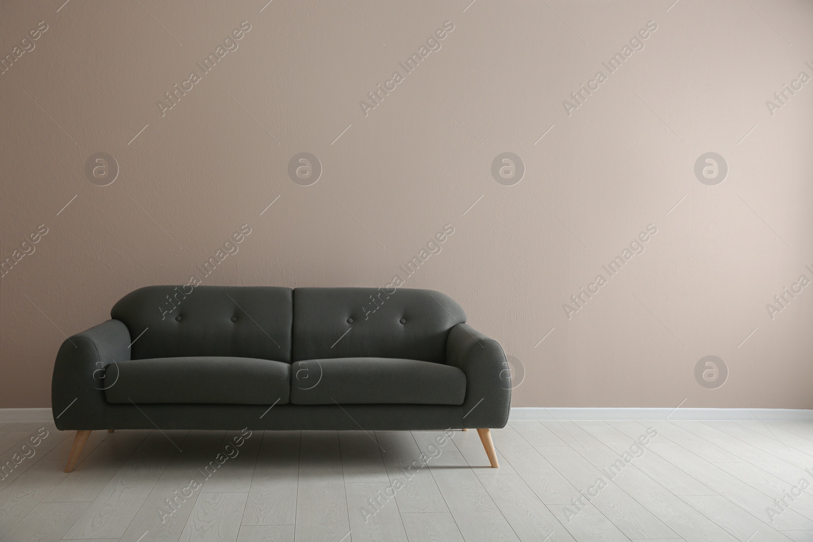 Photo of Comfortable grey sofa near beige wall indoors, space for text. Interior design