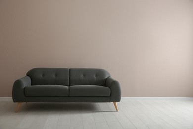 Photo of Comfortable grey sofa near beige wall indoors, space for text. Interior design