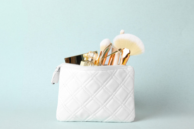 Cosmetic bag with makeup products and beauty accessories on light blue background