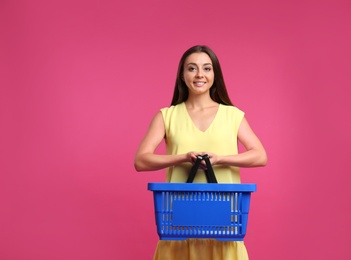 Young woman with empty shopping basket on pink background