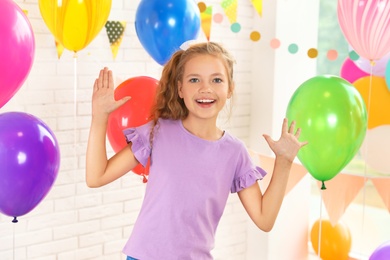 Happy girl near bright balloons at birthday party indoors