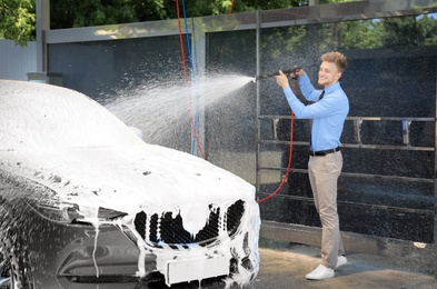 Photo of Businessman cleaning auto with high pressure water jet at self-service car wash