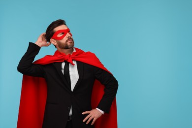 Photo of Businessman wearing red superhero cape and mask on light blue background. Space for text