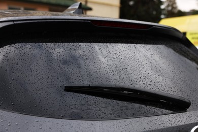 Photo of Car wiper cleaning water drops from rear windshield glass outdoors, closeup