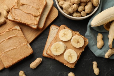 Photo of Tasty peanut butter sandwiches with sliced banana and peanuts on dark gray table, flat lay