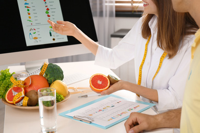 Photo of Young nutritionist consulting patient at table in clinic, closeup