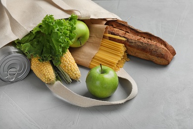 Shopping bag with fresh vegetables and other products on grey background