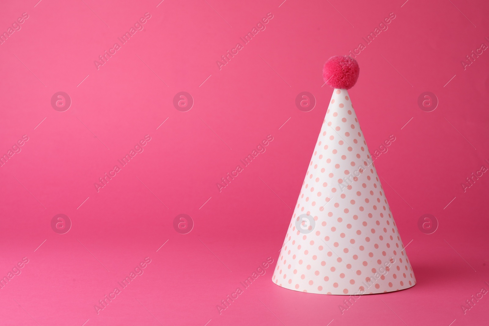 Photo of One beautiful party hat with pompom on pink background. Space for text