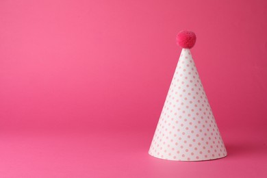 One beautiful party hat with pompom on pink background. Space for text