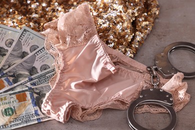 Photo of Prostitution concept. Women's panties, dollar banknotes and handcuffs on grey textured background