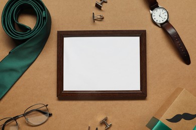 Photo of Empty photo frame, gift box and men accessories on brown background, flat lay with space for text. Father's day celebration