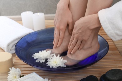 Photo of Woman soaking her feet in bowl with water and flowers on floor, closeup. Spa treatment