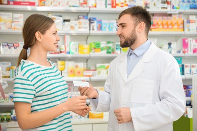 Photo of Professional pharmacist giving pills to customer in modern drugstore