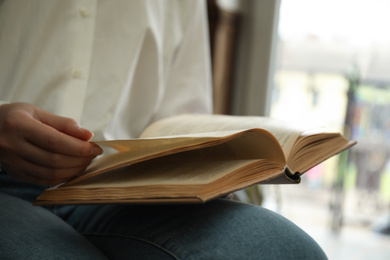 Photo of Woman reading book near window indoors, closeup