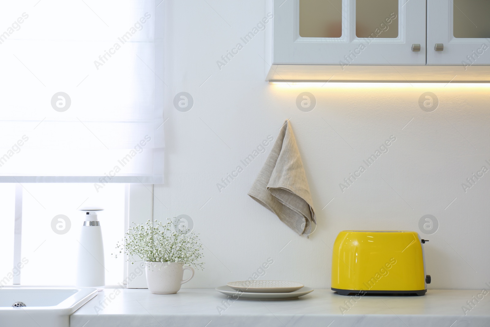 Photo of Modern toaster, plates and flowers on counter in kitchen