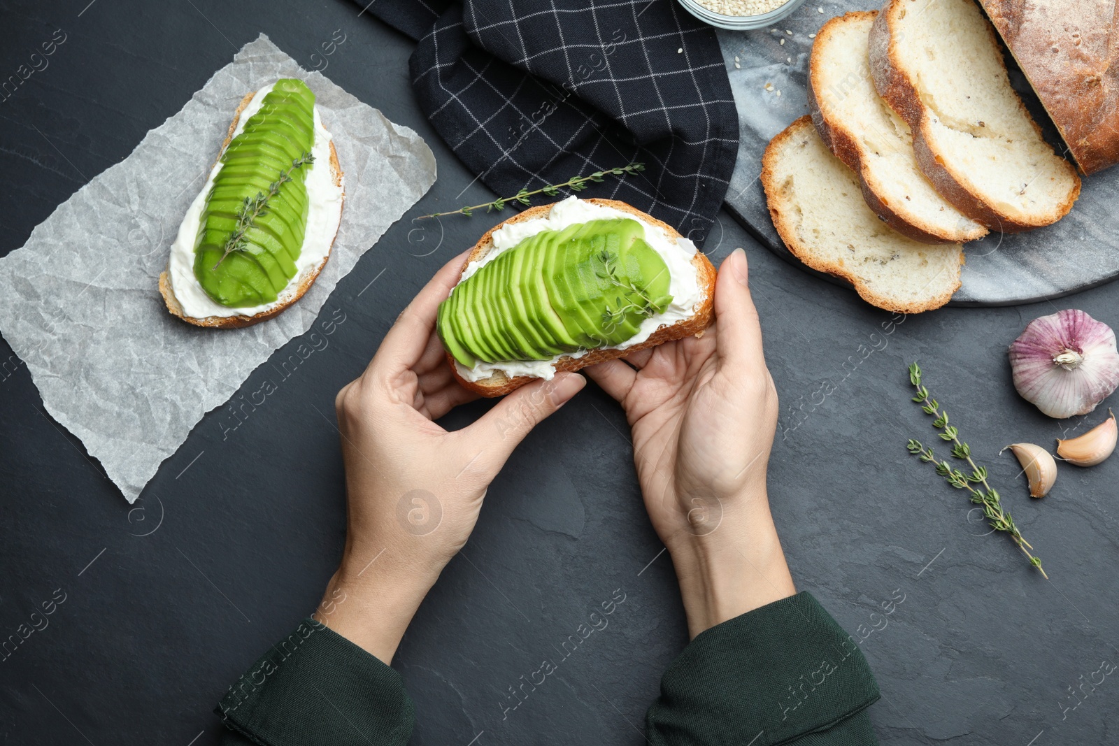 Photo of Woman holding tasty avocado sandwich at black table, top view