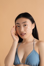 Photo of Beautiful young woman with sun protection cream on her face against beige background