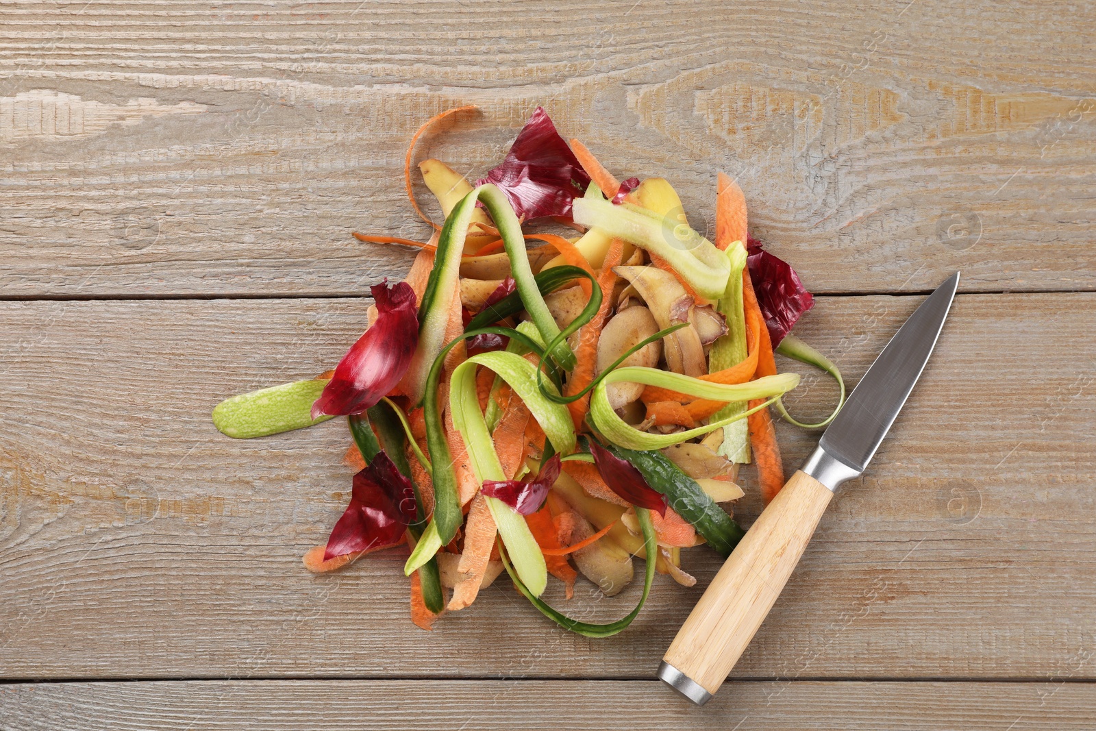 Photo of Peels of fresh vegetables and knife on wooden table, top view