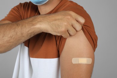 Photo of Vaccinated man showing medical plaster on his arm against grey background, closeup