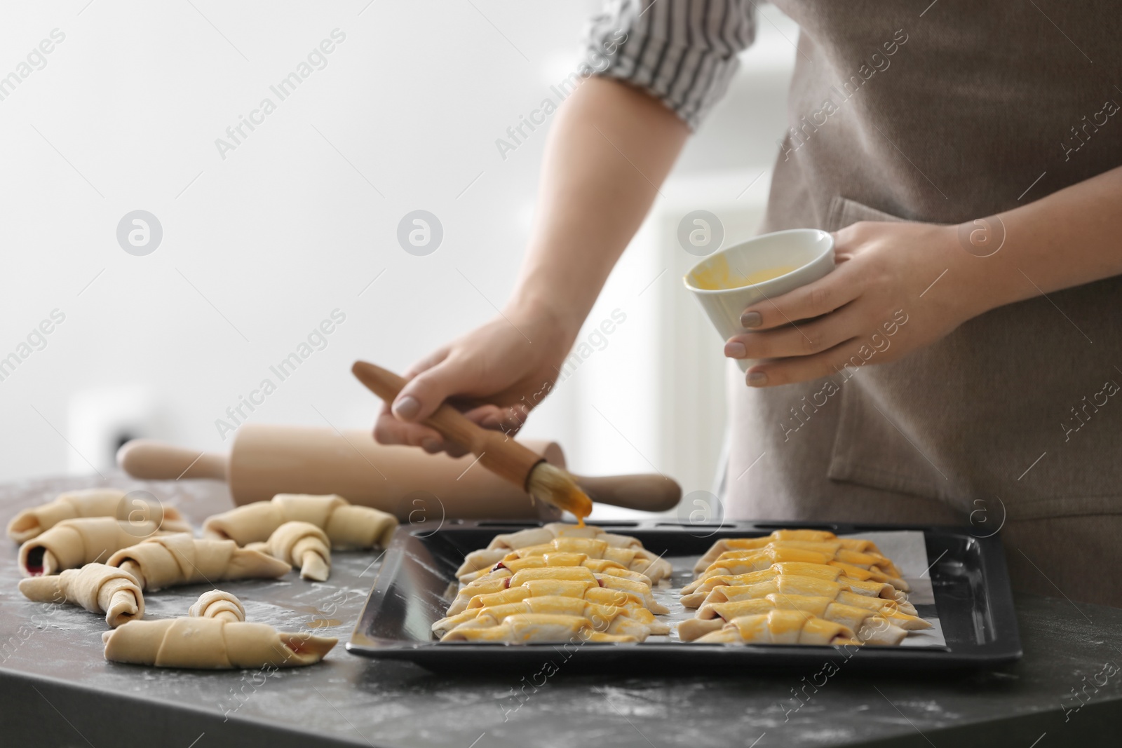 Photo of Woman spreading egg yolk on croissants, closeup