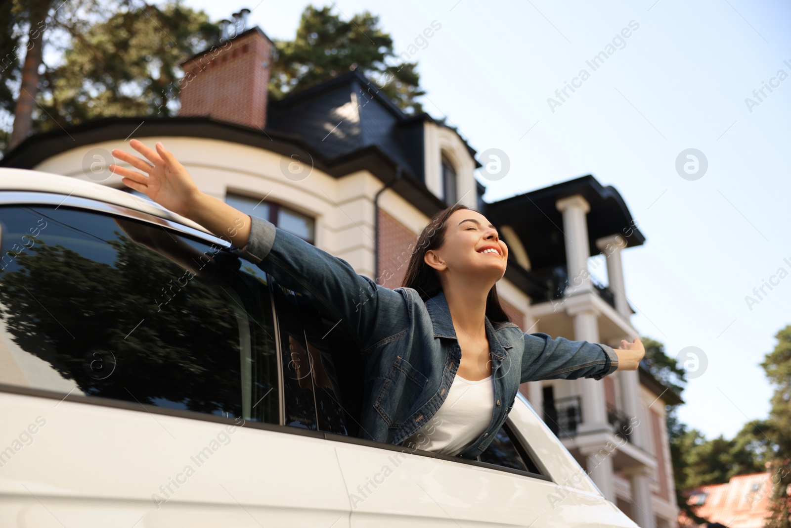 Photo of Happy young woman leaning out of window while enjoying car trip on city street, low angle view