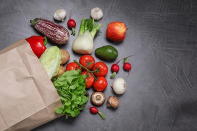 Photo of paper package with fresh vegetables and fruits on dark background, flat lay. Space for text