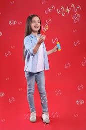 Photo of Little girl having fun with soap bubbles on red background