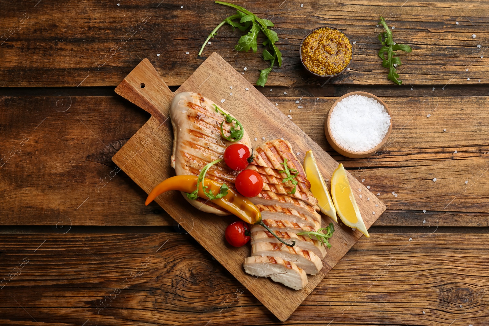 Photo of Tasty grilled chicken fillets with tomatoes, lemon slices  and chili pepper on wooden table, flat lay