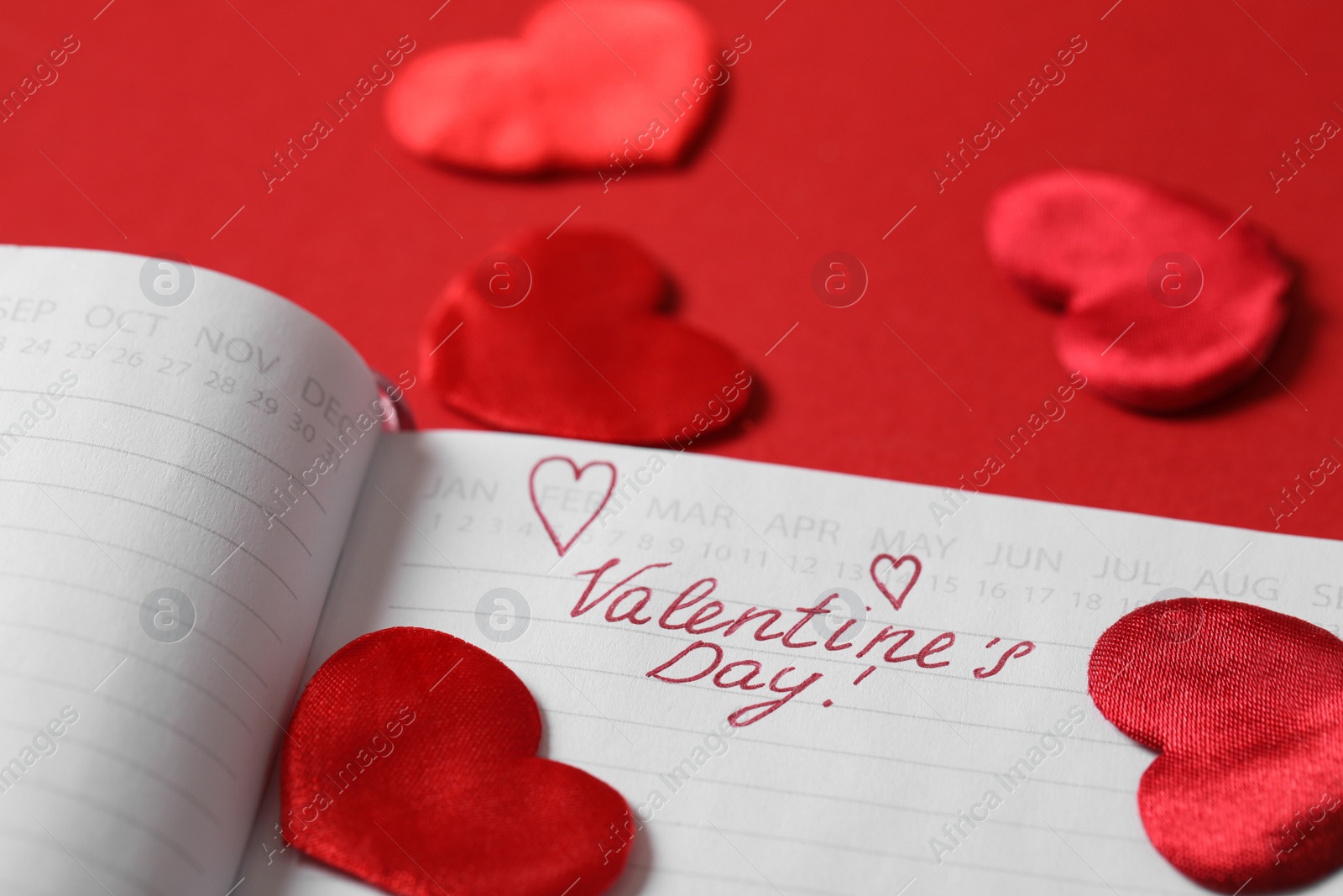 Photo of Notebook with text Valentine's Day and hearts on red background, closeup