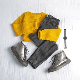 Flat lay composition with jeans, sweater and shoes on white fabric