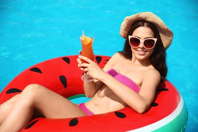 Photo of Beautiful young woman with cocktail and inflatable ring in swimming pool