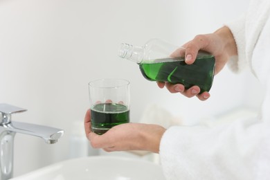 Photo of Young man using mouthwash in bathroom, closeup