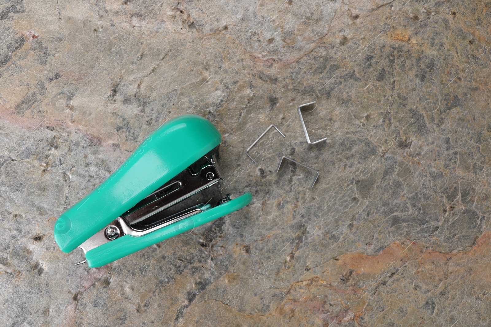 Photo of Turquoise stapler with staples on stone textured surface, top view. Space for text