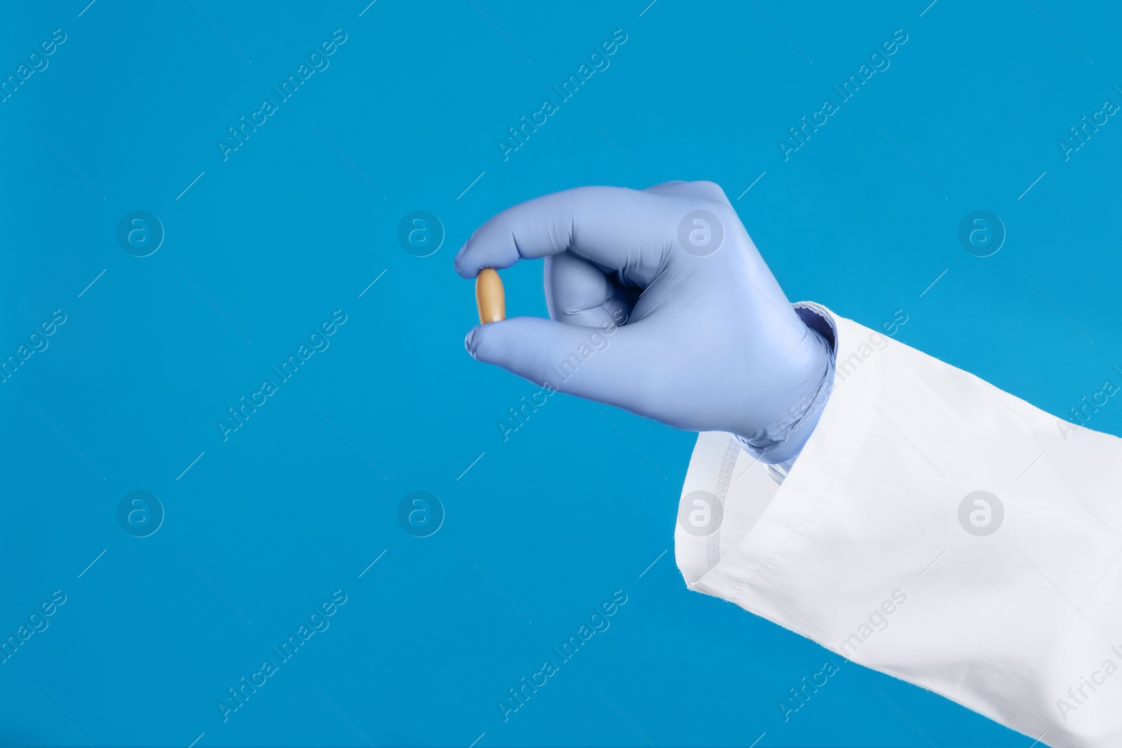 Photo of Doctor holding suppository for hemorrhoid treatment on blue background, closeup