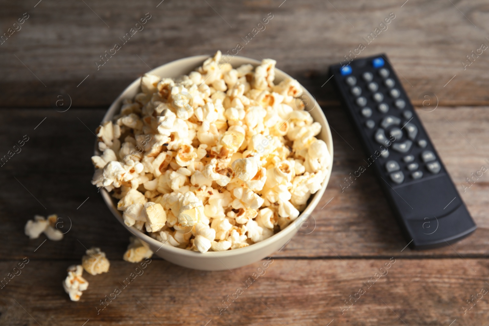 Photo of Bowl of popcorn and TV remote on wooden background. Watching cinema