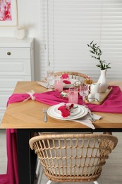 Photo of Color accent table setting. Glasses, plates, pink napkins and vase with green branch in dining room