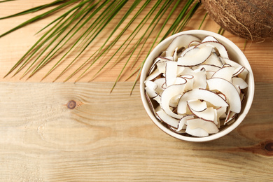 Photo of Tasty coconut chips on wooden table, flat lay. Space for text