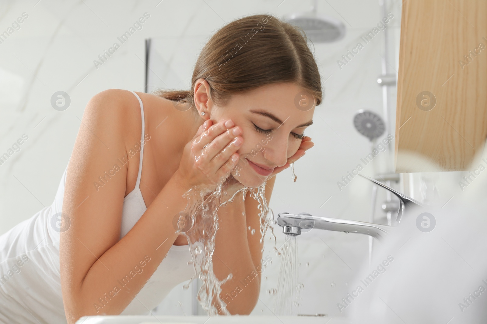 Photo of Young woman washing her face with water in bathroom